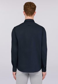 Camicetta blu navy a maniche lunghe con colletto, polsini con bottoni e una texture liscia. La vista posteriore mostra un orlo curvo e dettagli di branding minimi.