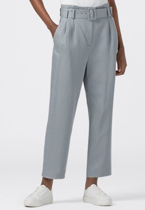 Pantalons larges gris clair avec taille haute ceinturée, devant plissé et deux poches latérales. Portés avec des baskets blanches.
