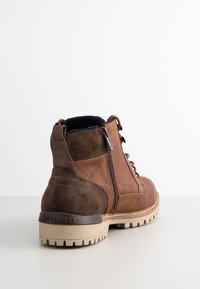 Brown leather ankle boots with suede accents, featuring a side zipper, lace-up front, textured sole, and a branded heel.