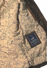 Intérieur d'une veste en cuir marron avec une doublure en tissu beige imprimée d'une carte détaillée de la France et une petite étiquette dans le coin inférieur.