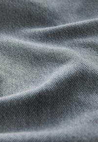 Lys grå denimstof med en glat tekstur, der har subtile vævemønstre og blide bølger, hvilket fremhæver dets bløde, fleksible natur.