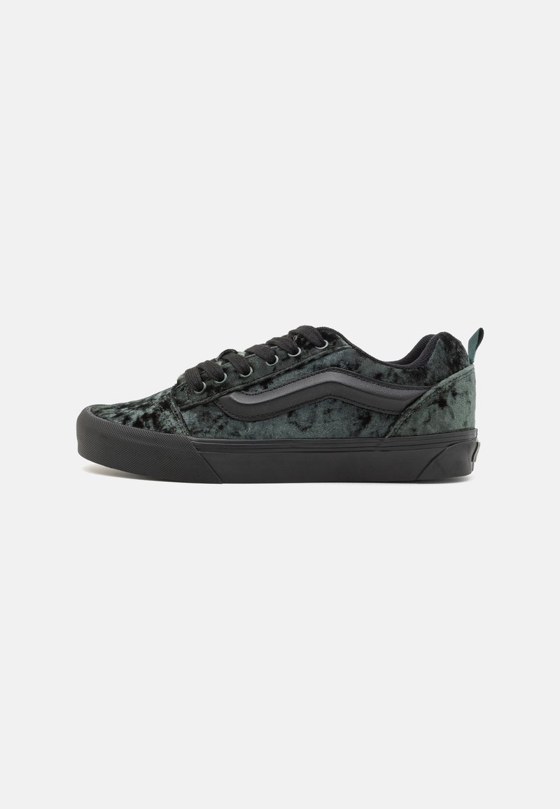Adidași din catifea neagră cu o suprafață texturată, cusături albe, șireturi negre și o talpă din cauciuc. Prezintă un design clasic cu dungi pe lateral.