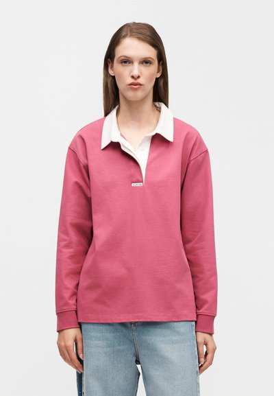 Ροζ μακρυμάνικο πόλο με λευκό γιακά, με V λαιμόκοψη και μικρή λεπτομέρεια λογότυπου στο στήθος, κατασκευασμένο από απαλό ύφασμα.