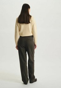 Pull beige et pantalon rayé sombre. Le pull est doux, avec des manches ajustées. Le pantalon est bien coupé, avec une taille visible et des poches.