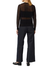 Schwarzer transparenter Pullover mit langen Ärmeln und geripptem Saum, kombiniert mit dunkelblauen weit geschnittenen Jeanshosen und schwarzen flachen Schuhen.