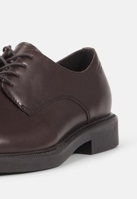 Chaussure en cuir marron à lacets avec une texture lisse, un cap-toe arrondi et un petit talon carré. Détails de couture subtils le long des bords.
