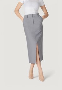 Falda de lápiz gris con un corte lateral, ajuste entallado, tejido suave, de longitud media y con passadores para cinturón, combinada con una blusa blanca ajustada y tacones beige.