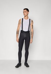 Schwarze Radsport-Bib-Tights mit Trägern, ausgestattet mit einer glatten Textur, figurbetontem Design und einem kontrastierenden weißen Mesh-Top darunter.