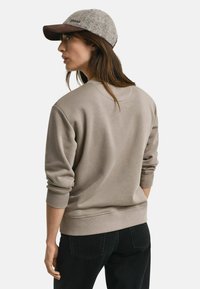 Beige sweatshirt met een relaxed fit en geribbelde manchetten, gecombineerd met een grijze pet met een bruine rand. Eenvoudig ontwerp zonder zichtbare logo's.