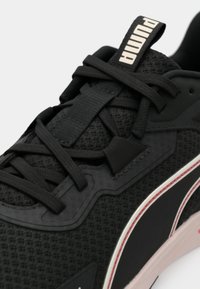 Κοντινό πλάνο μαύρου αθλητικού παπουτσιού Puma με ύφασμα από δίχτυ, μαύρα κορδόνια, ταμπελάκι με το λογότυπο και λεπτομέρειες στη σόλα σε άσπρο και κόκκινο.