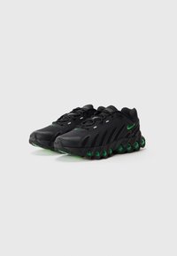Baskets de sport noires avec une tige synthétique texturée, accents verts sur la semelle et le logo, dotées d'un design de talon arrondi et sculpté.