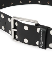 Fekete bőr öv nagy ezüst szegecsekkel, ezüst fém csattal és egy címkével, amelyen a "KARL LAGERFELD JEANS" felirat található fekete betűkkel.