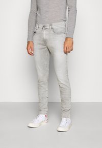 Vaqueros gris claro de corte ajustado con cinco bolsillos, textura ligeramente desvaída y cinturilla estándar. Combinados con zapatillas altas blancas.