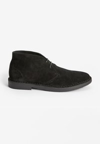 Black suede ankle boots with a pointed toe, two eyelets for laces, and a stitched rubber sole. Smooth texture and minimalist design.