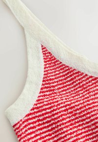 Gros plan d'un haut sans manches en maille texturée rouge et blanche avec une bordure blanche le long de l'encolure et de la bretelle.