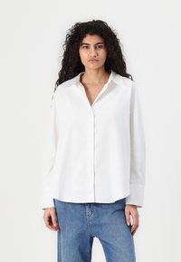 Witte lange mouwen overhemd met knopen, gemaakt van lichte stof. Heeft een klassieke kraag, een ontspannen pasvorm en een afgeronde zoom. G gedragen met denim broek.