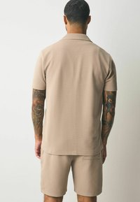 Beige short-sleeve polo shirt with a textured striped design, paired with matching shorts featuring a back pocket. Smooth fabric.