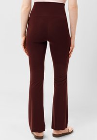 Hoog getailleerde bordeauxrode flared leggings gemaakt van rekbare stof. Zachte textuur zonder zichtbare patronen. Gestyld met lichte schoeisel.