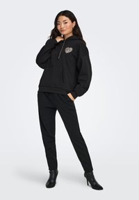 Sudadera negra con capucha con bolsillo canguro y diseño de corazón con patrón de cebra; combinada con pantalones negros ajustados y botines de tacón.