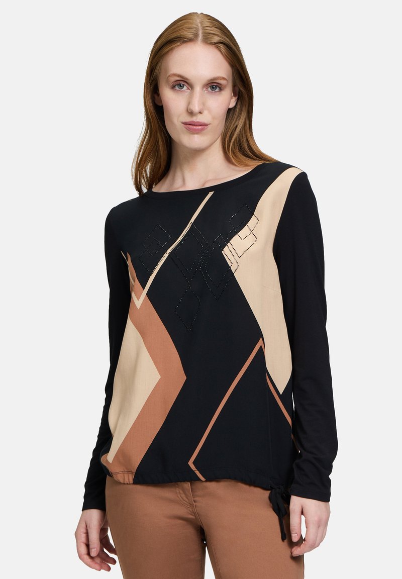 Langärmliges Oberteil mit schwarzen, sandfarbenen und braunen geometrischen Mustern, verziert und mit einem Kordelzug am Saum. Glatte Stofftextur.