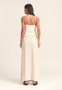 Beige satin camisole med tynde stropper parret med en matchende lang nederdel med et geometrisk design. Glat tekstur, minimal hardware, slank silhuet.