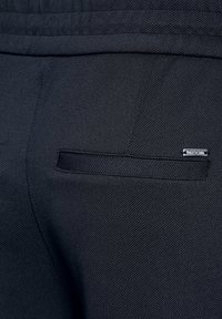 Pantaloni neri su misura con tessuto strutturato, dotati di una piccola tasca posteriore e un dettaglio in metallo vicino alla cucitura della tasca.