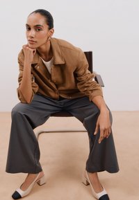 Ruskea mokkainen takki, jossa on näkyvät napit, valkoinen t-paita, harmaat leveälahkeiset housut ja kahden sävyn slingback-kengät, joissa on tukeva korko.