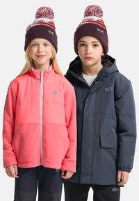 Zwei Kinder tragen Outdoor-Jacken, eines in leuchtendem rosa Fleece und das andere in dunkelblauer, wasserdichter Stoff. Beide haben Strickmützen mit Bommel.
