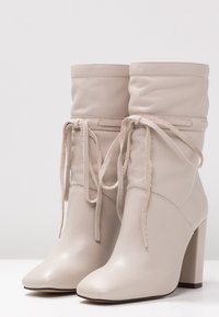 Bottes à cheville en cuir beige au design décontracté, bout pointu et talon épais carré. Dotées de lacets et d'accents minimalistes.