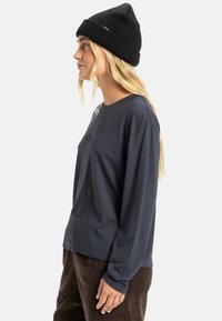Langermet marineblå skjorte med rund hals, sammen med strukturerte brune kordfløyelsbukser. Modellen har på seg en svart strikket lue.