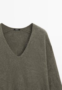 Vokuhila-Pullover aus einem weichen, olivgrünen Strick. Mit lockeren Ärmeln und einem entspannten Schnitt, der eine gemütliche Textur betont. Markenlabel sichtbar.