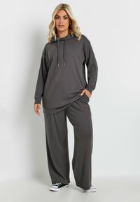 Grå ribbat hoodie med dragsko och långa ärmar, i kombination med vida byxor. Texturerad tyg med avslappnad passform, kompletterad med svarta sneakers.