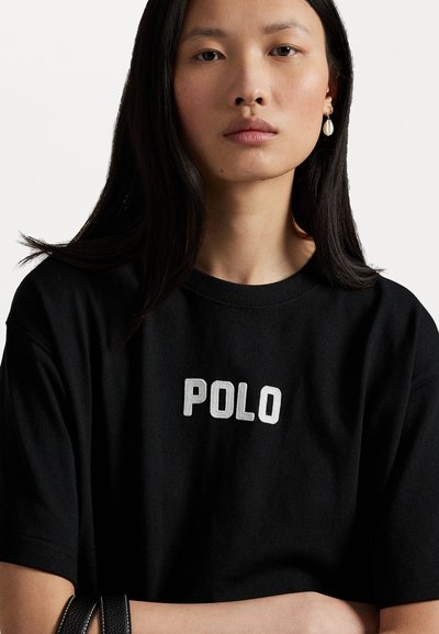 Tricou din bumbac negru, cu mâneci scurte și decolteu rotund, având un logo alb "POLO" într-un font îndrăzneț pe piept.