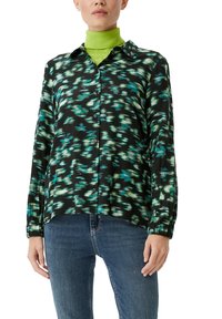 Black shirt with a green and blue abstract pattern, button-down design, long sleeves, and a relaxed fit. Worn over a green turtleneck.
