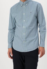 Camicia a scacchi verde e blu navy con colletto, maniche lunghe e bottoni bianchi. Presenta un piccolo logo sul lato sinistro del petto.