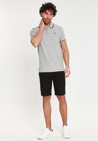 Grå polo-shirt med krave, og med kontrasterende rød trim. Båret med sorte shorts og hvide sneakers. Enkel, klassisk design.