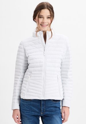 Weiße Daunenjacke mit horizontaler Steppstruktur, hohem Kragen und mit Reißverschlüssen versehenen Taschen, kombiniert mit blauen Jeans.