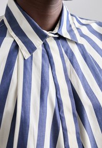 Blue and white striped shirt featuring a classic collar, cotton fabric, and pleated design for added texture and structure.