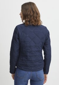 Jachetă de nave, matlasată, cu model în diamond, având guler rotund și mâneci lungi, asortată cu blugi din denim albastru.