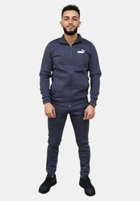Tuta navy realizzato in un materiale liscio con giacca con zip e pantaloni aderenti, con il logo Puma sul petto e sulla coscia.
