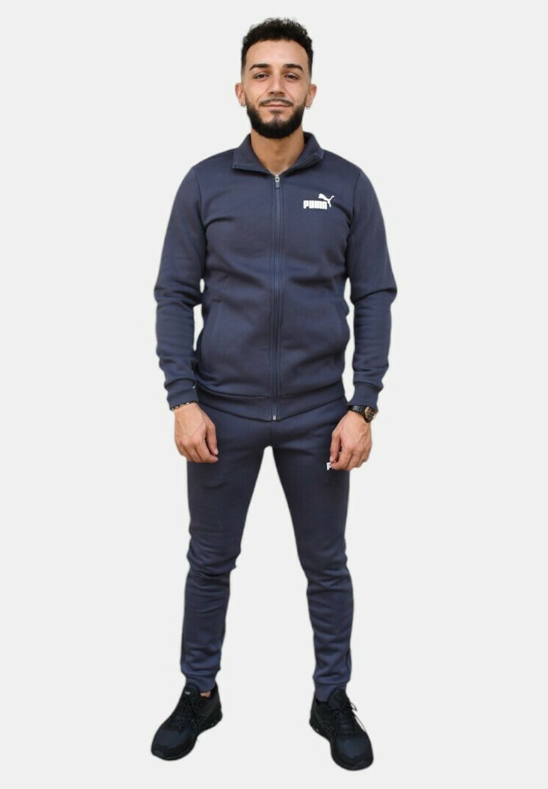 Tuta navy realizzato in un materiale liscio con giacca con zip e pantaloni aderenti, con il logo Puma sul petto e sulla coscia.