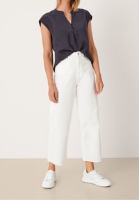 Blouse texturée bleu marine avec des manches courtes et un col fendu, associée à un pantalon large blanc et des baskets blanches. Tenue simple et décontractée.