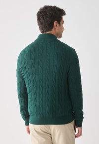 Donkergroen kabelgebreid sweater, lange mouwen, ribgebreide kraag en zoom, textuurpatroon op de rug, gemaakt van zachte, rekbare stof.