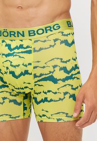 Björk Borg vīriešu bokseri spilgti dzeltenā krāsā ar tumši zaļiem mākoņu rakstiem, izgatavoti no elastīga materiāla, ar zaļu zīmola jostasvietu.