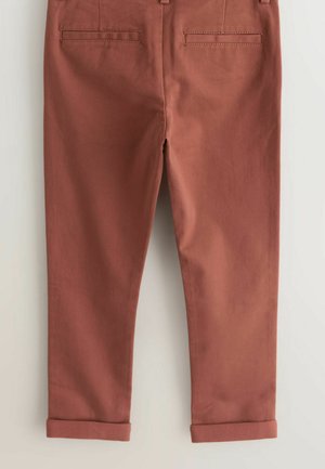 Pantaloni color ruggine con orli risvoltati e due tasche a filetto sul retro, mostrati distesi su uno sfondo chiaro.