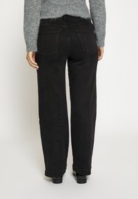 Crne traperice visokog struka sa ravnim nogavicama, s dvije stražnje džepa i vidljivim šavovima duž šavova. Teksturirani materijal.