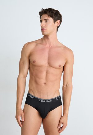 Schwarze Calvin Klein Unterhosen mit einem weichen elastischen Bund, der mit weißen Marken Schriftzügen verziert ist. Fitted Design, glatte Textur und minimale Details.