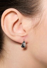 Kolczyki w kształcie kropli o błyszczącej czarnej powierzchni z przezroczystym akcentem kamienia szlachetnego. Wykonane z metalu, zwisają z płatka ucha.