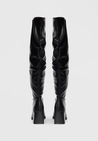 Bottes noires en cuir, arrivant jusqu'au genou, au design décontracté, avec un talon carré et une texture lisse. Fermeture zippée à l'arrière pour un enfilage facile.
