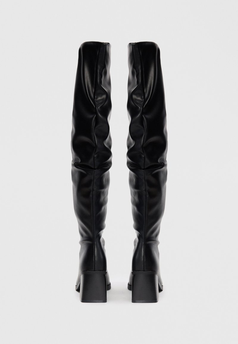 Bottes noires en cuir, arrivant jusqu'au genou, au design décontracté, avec un talon carré et une texture lisse. Fermeture zippée à l'arrière pour un enfilage facile.